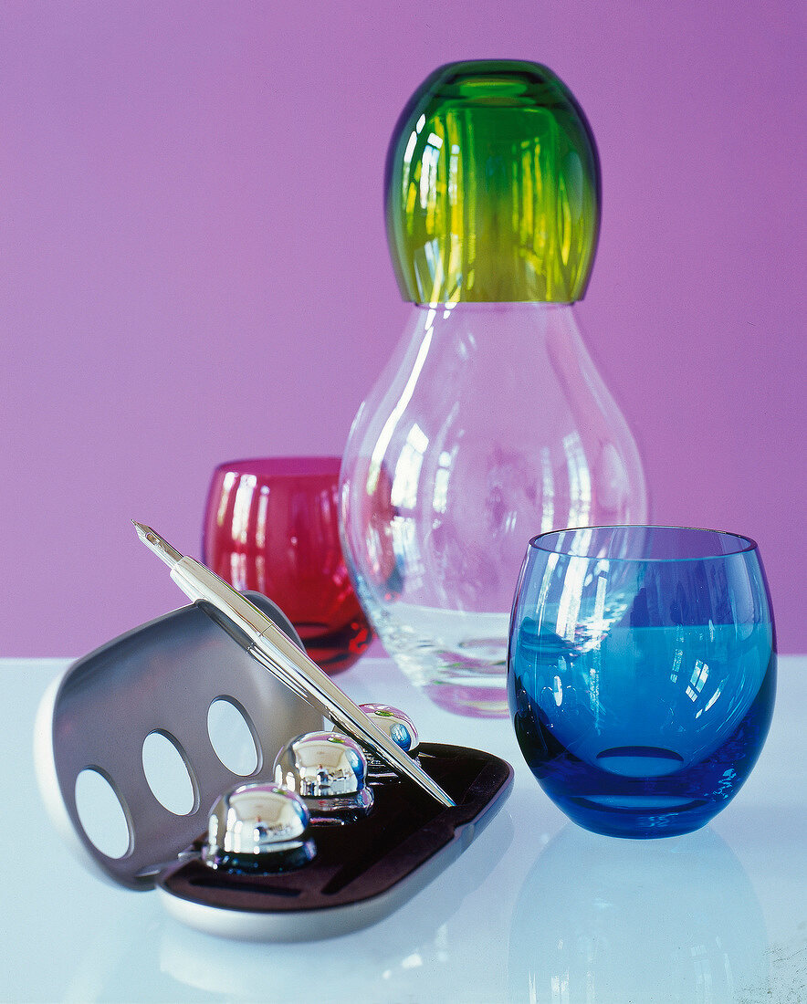 Glass carafe, green, red and blue glass cups with schreibbox on glass table