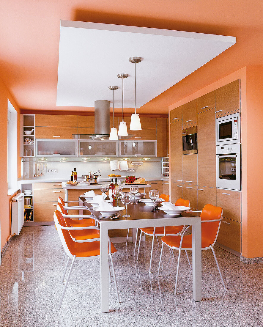 View of orange kitchen with several cabinets and tableware on dining table