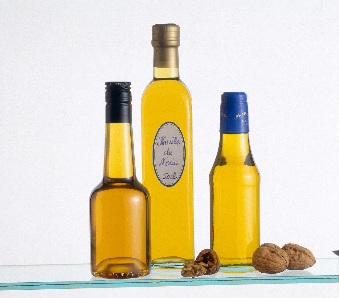 Different types of nut oils in glass bottles on white background