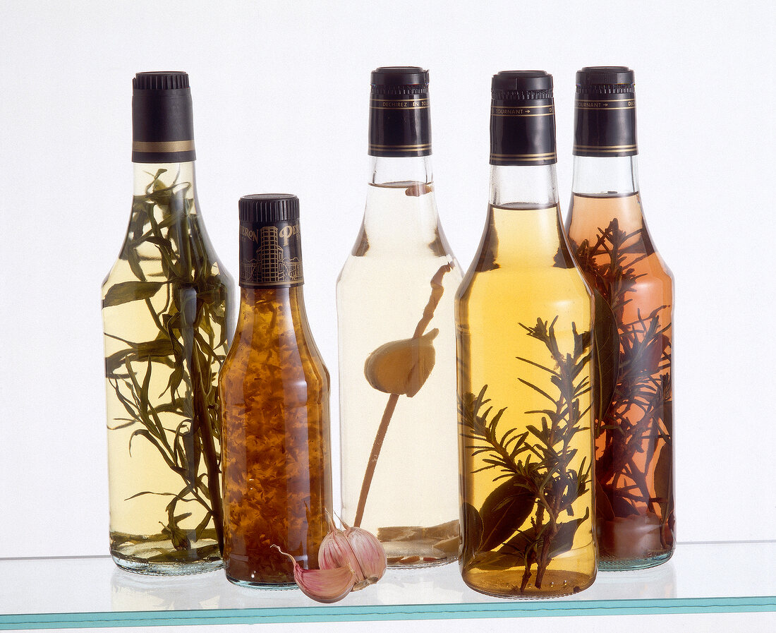 Different types of herbal vinegars in glass bottles on white background