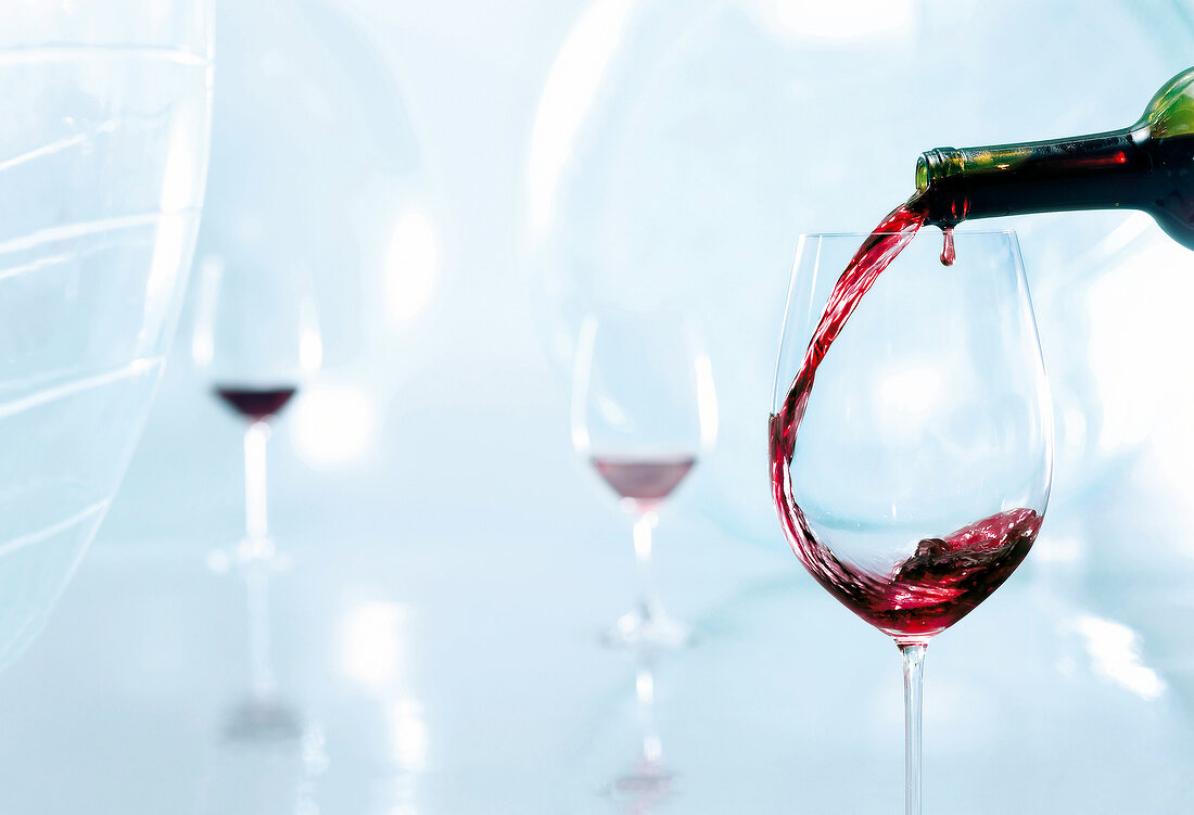 In ein Weinglas wird Rotwein eingeschenkt