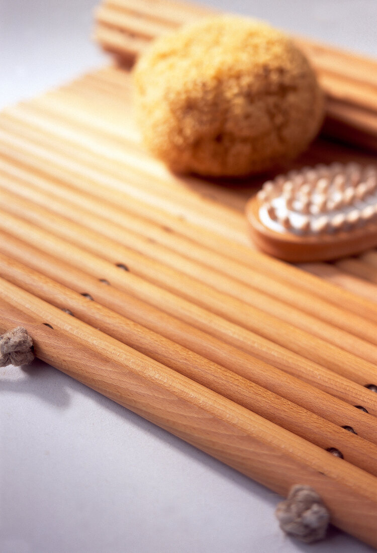 Close-up of brown sponge and massage brush placed on mat made of beech wood