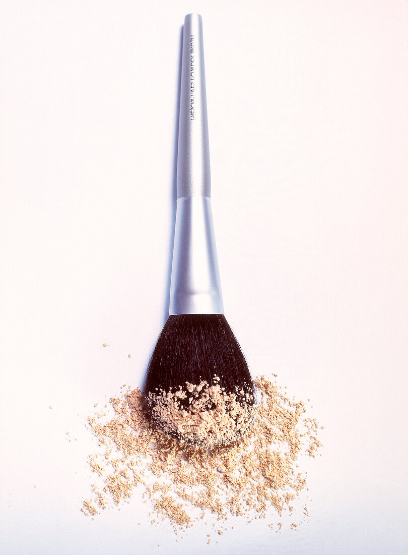 Silver brush with make-up powder spread on bristles against white background