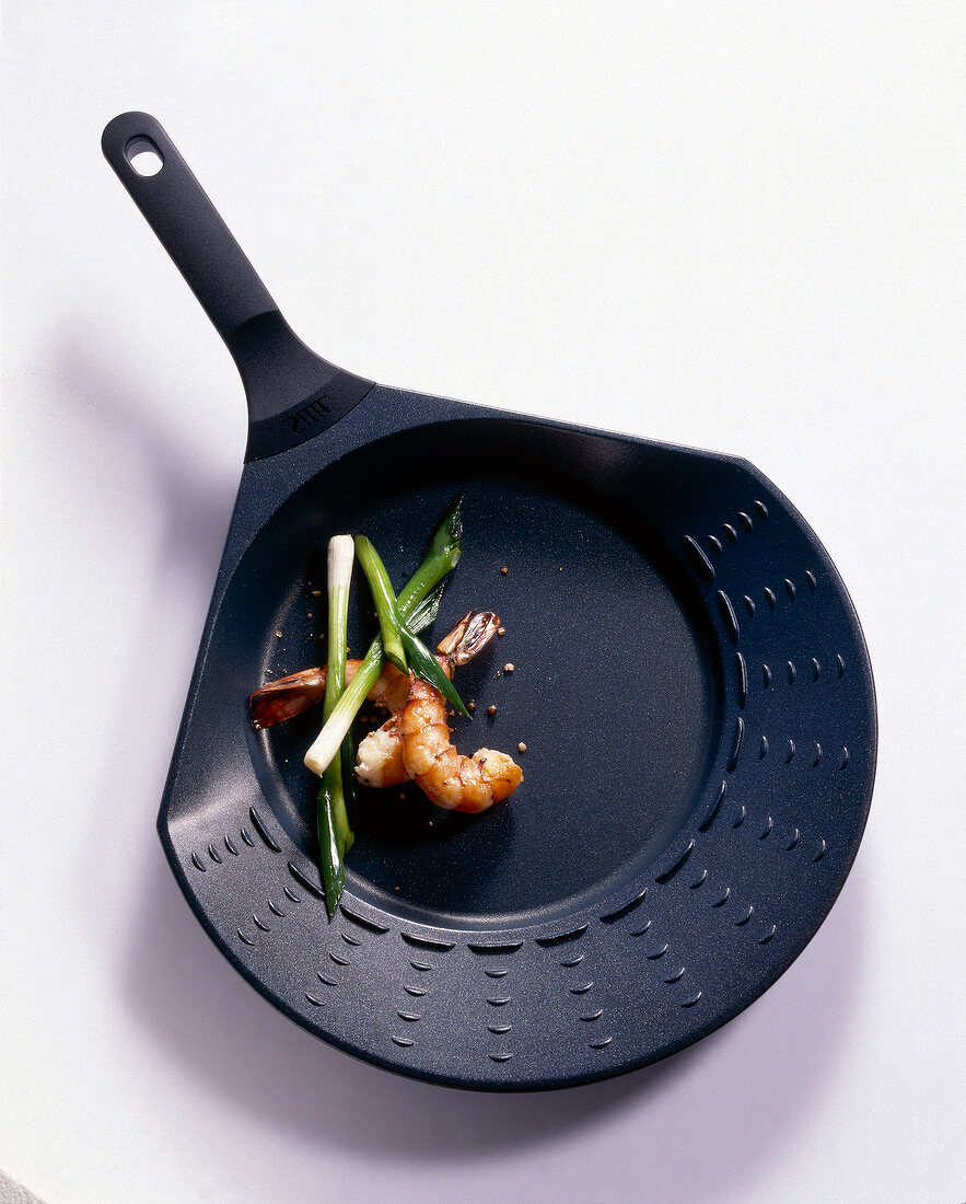 Shrimp and leek in a shallow fry pan on white background, overhead view
