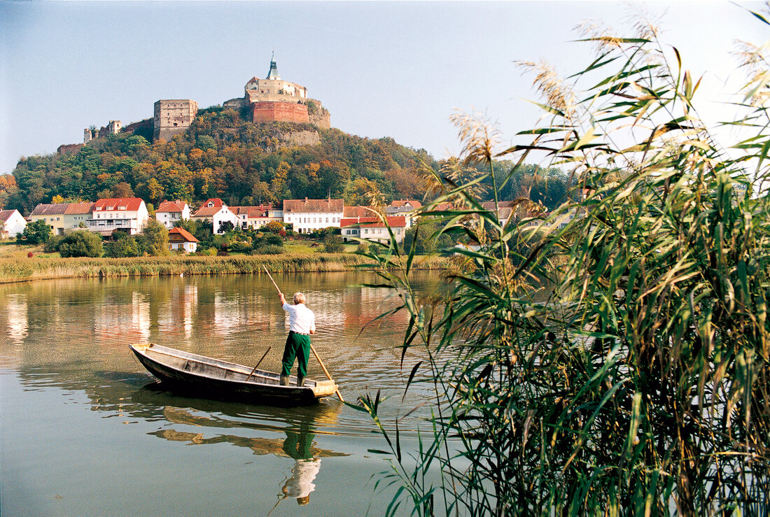 Ein Mann im Boot auf dem Fluss, im Hintergrund eine Burg und Häuser.