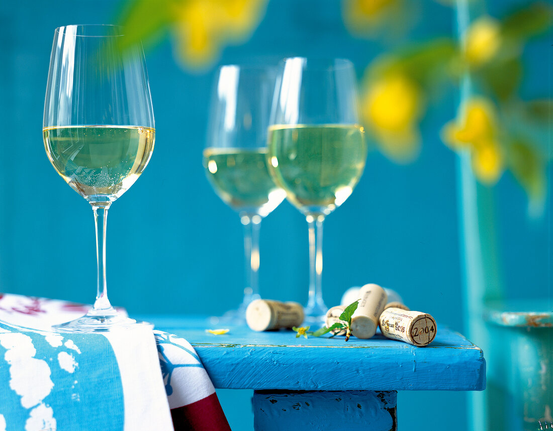 Three wine glasses with white wine and corks on table