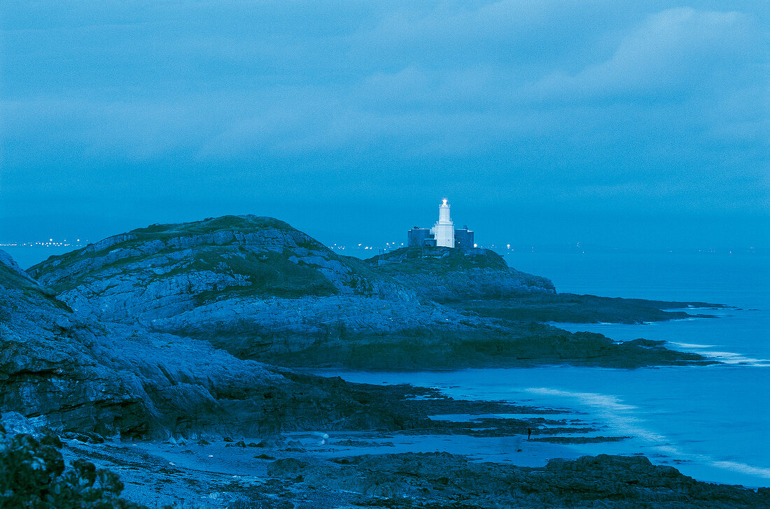 Leuchtturm, Felsküste, in der Ferne Lichter des Badeortes The Mumbles