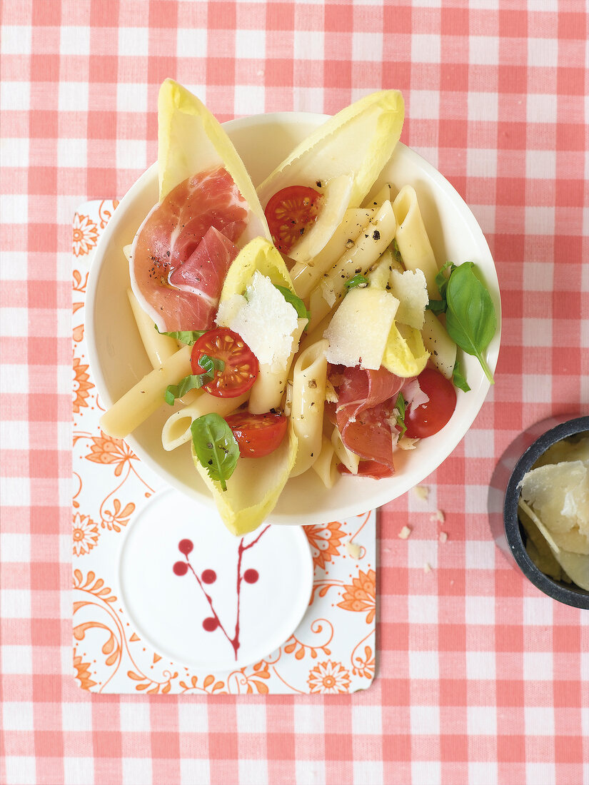 Penne chicory salad with cherry tomatoes, parma ham and basil in bowl