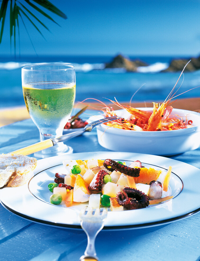 Fresh seafood salad on a plate, shrimp in bowl and glass of white wine on table