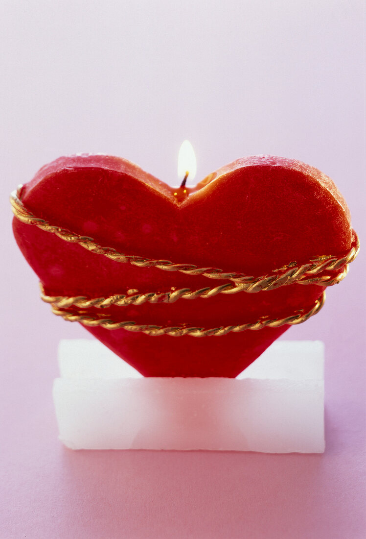 Heart shape candle wrapped with ribbon against pink background