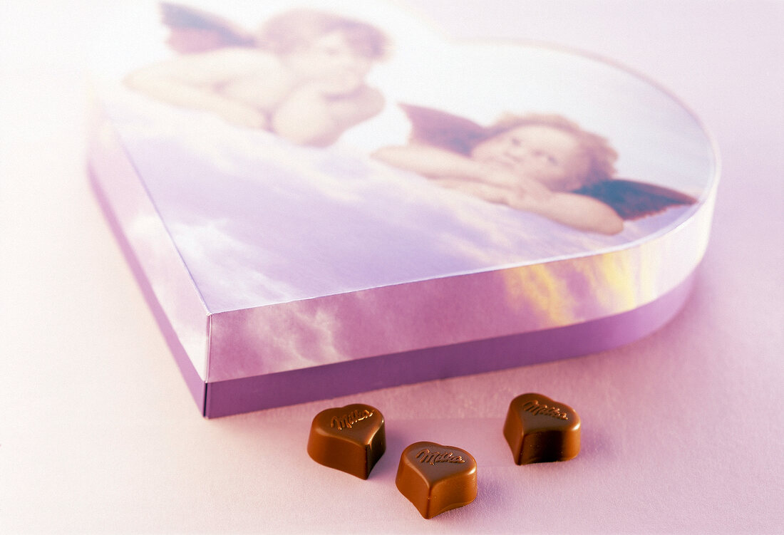 Box of chocolates and three heart shaped chocolates on pink surface