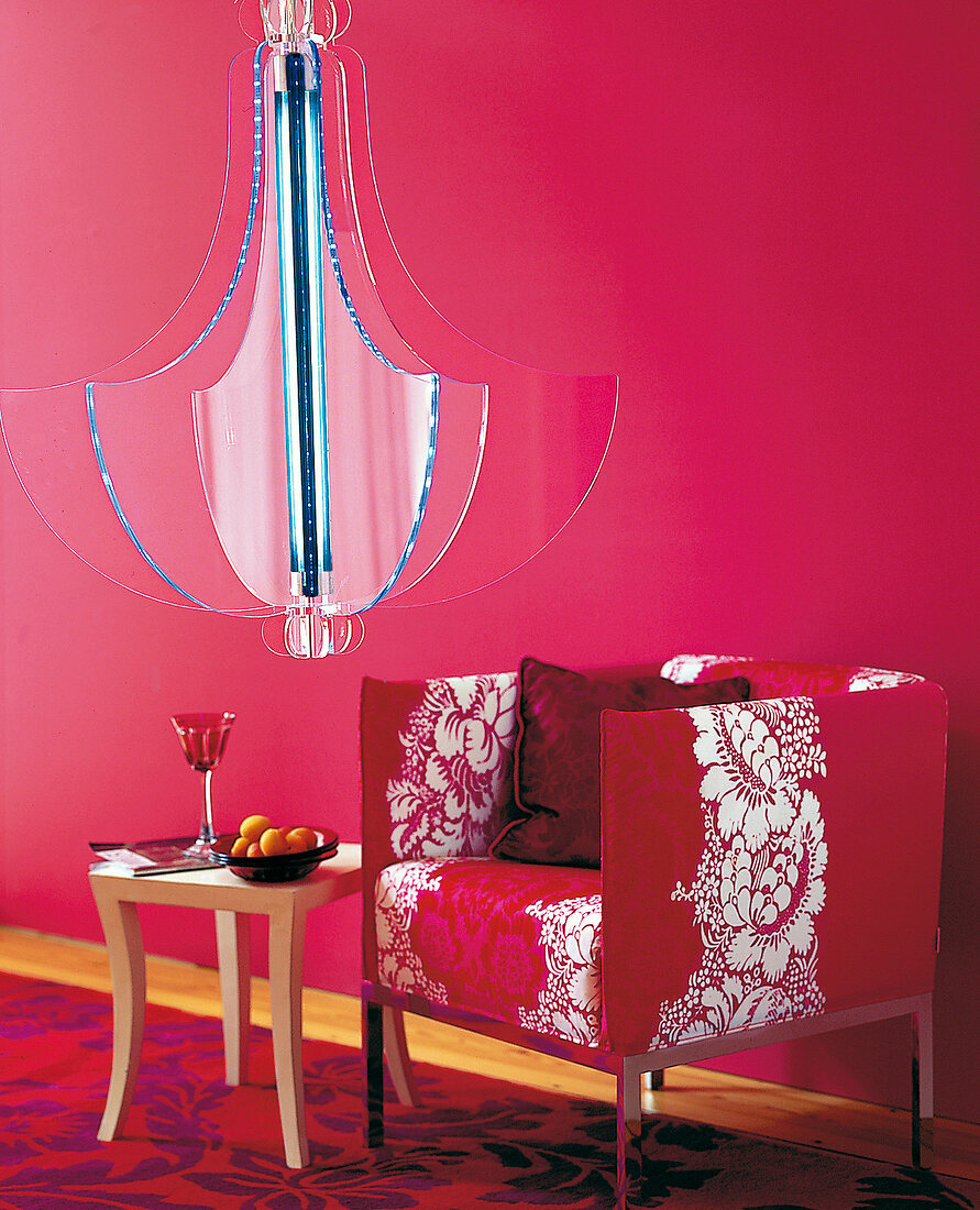 Roter Sessel mit Blumenmotiv, kleiner Tisch und Hängeleuchte.