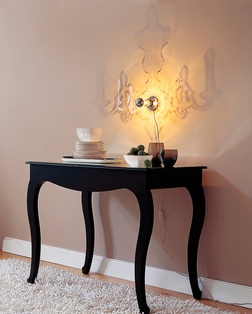 Acrylglas-Leuchte und dunkler Tisch vor beiger Wand.