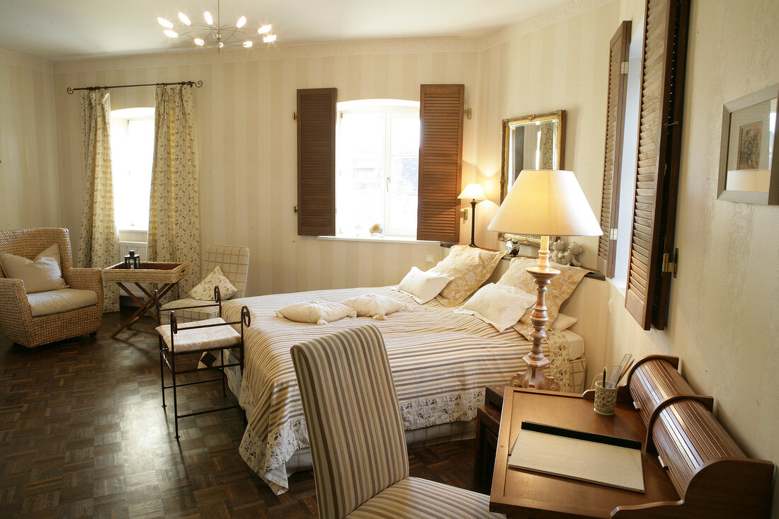 Interior of bedroom with bed, cushion, chairs, tables and chandelier in hotel