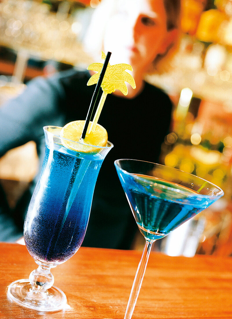 Blaue Cocktails mit Zitronenscheibe und Sternanis, Frau im Hintergrund