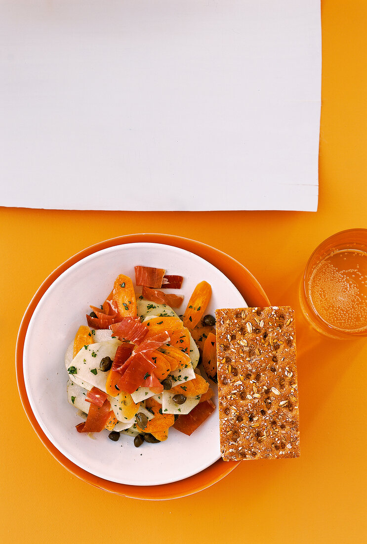 Kohlrabi and carrot salad with capers and crunchy crisp bread ham on plate, overhead view