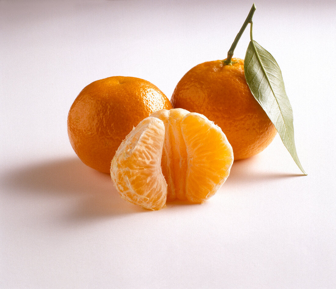 Two whole oranges and one peeled orange on white background