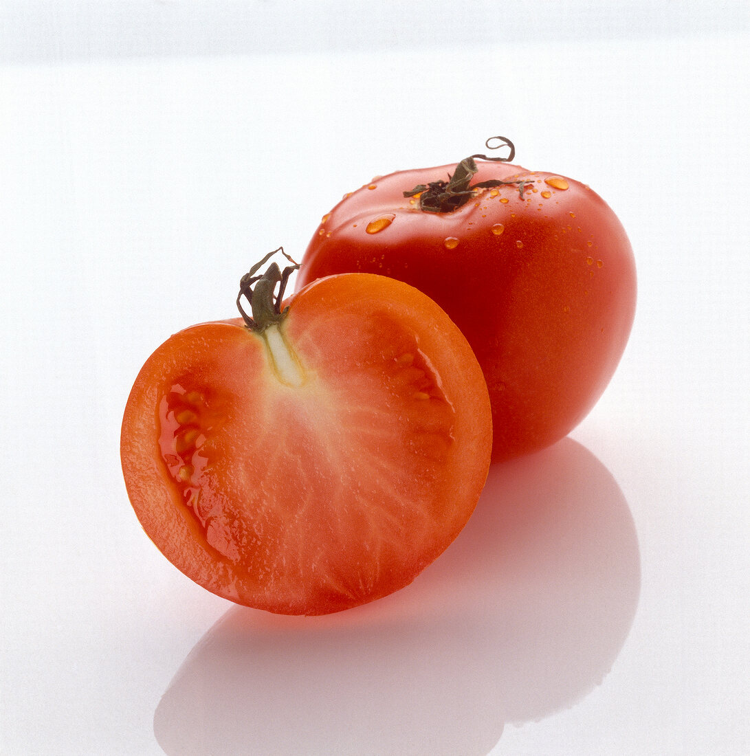 One whole and one sliced tomato on white background
