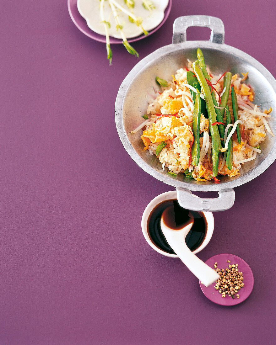 Fried rice with stir fried vegetables in wok on purple background, copy space