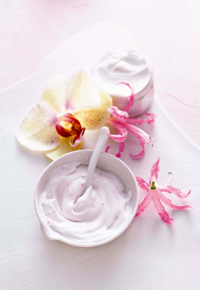 Close-up of white bowl with cream, cream container and three flowers on white background