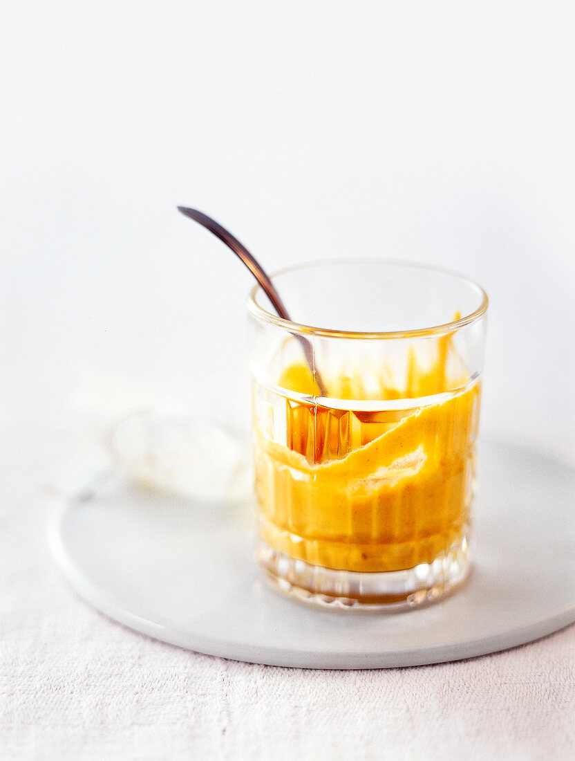 Glass with mustard paste and spoon on plate