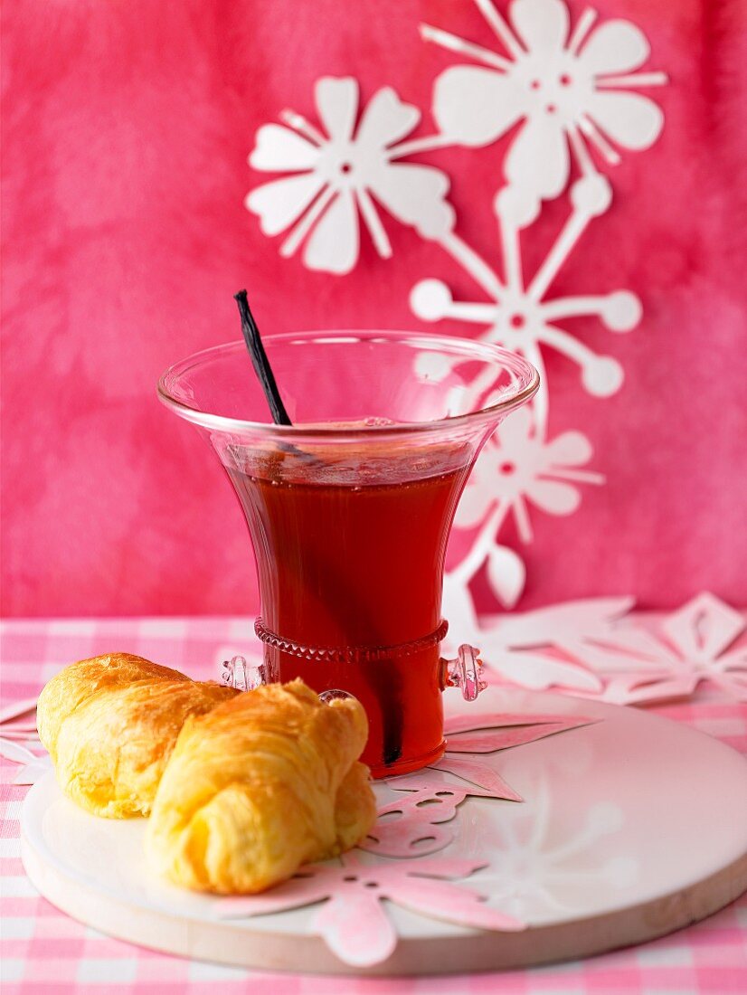 A glass of strawberry and rhubarb jelly with champagne and a croissant