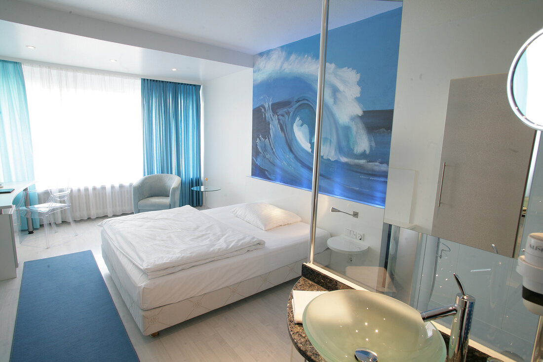 Room with bed, arm chair, white curtains and picture frame on wall at hotel in Germany