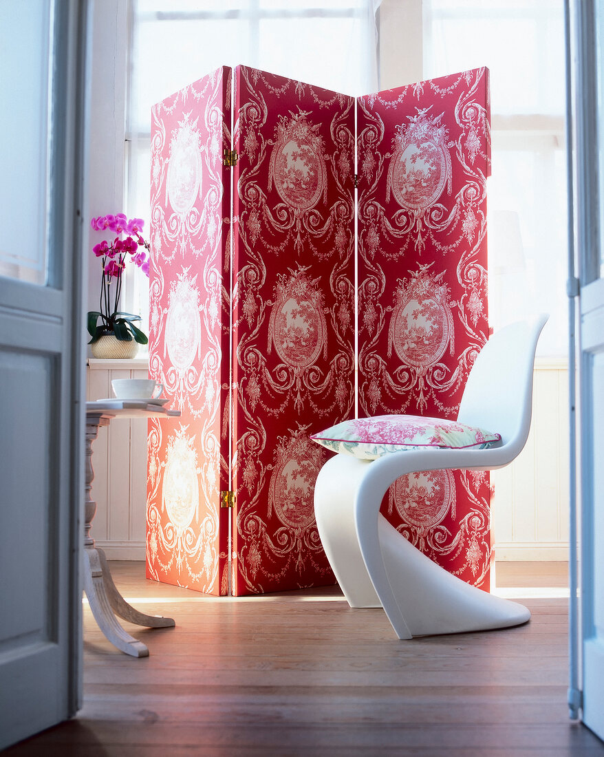 Cushion on modern chair and room divider with Toile de Jouy pattern in red against window