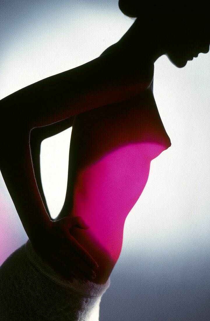 Silhouette of nude woman with pink light on abdomen