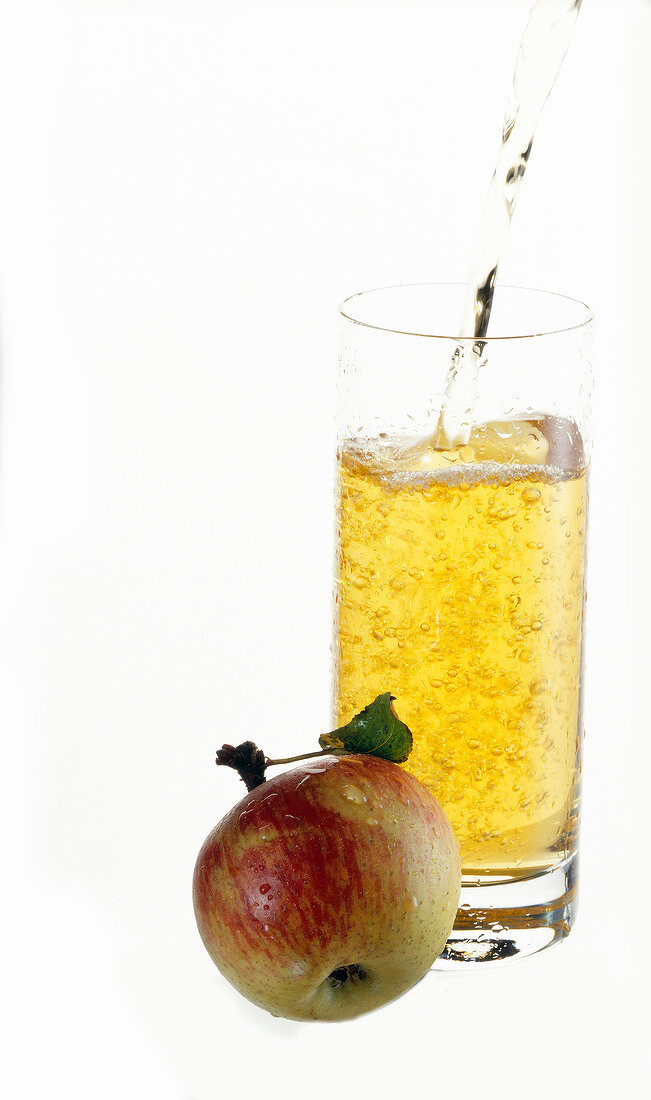Apfelschorle wird in ein Glas gegossen, davor liegt ein Apfel