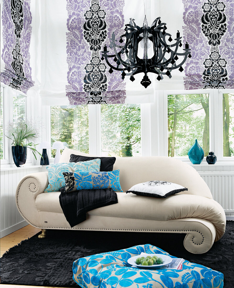 Colourful pillows on beige colour sofa with chandelier and curtain against window