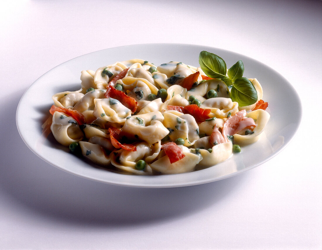 Tortellini with ham, peas and basil on plate