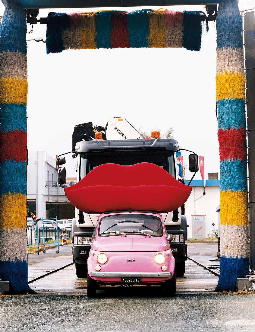 Red lips shaped designer sofa loaded on pink car in front of large truck