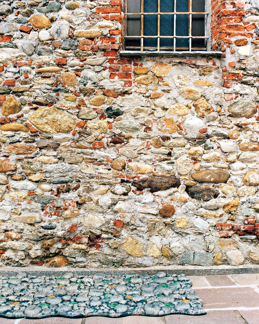 alte Kirchenmauer aus Naturstein, davor kunstvoller Teppich, Kunst