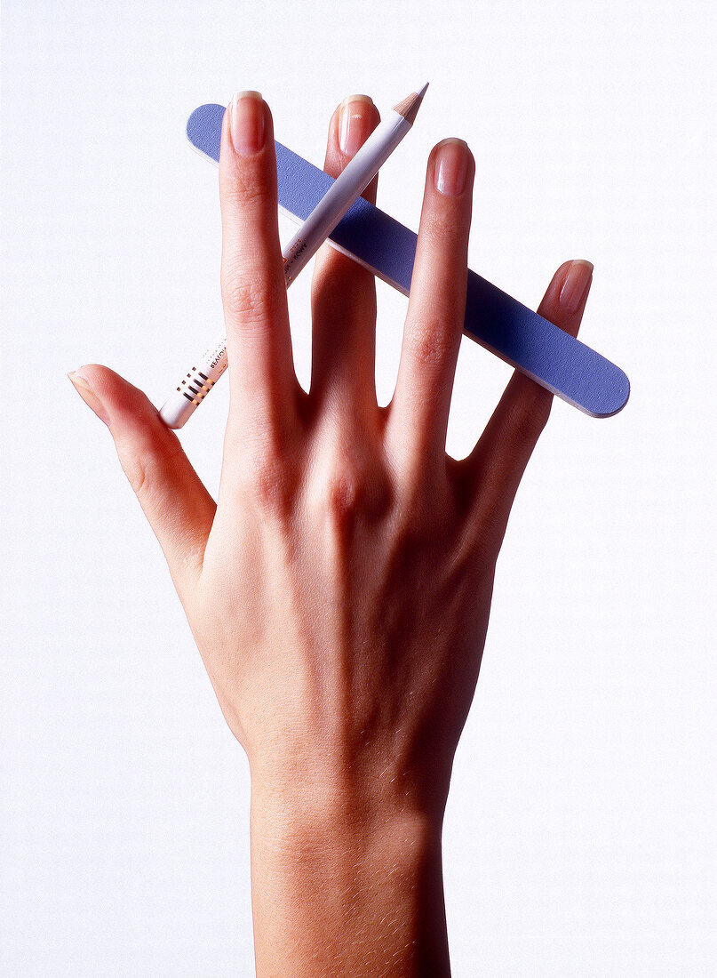 Close-up of woman holding nail file and white pen between fingers