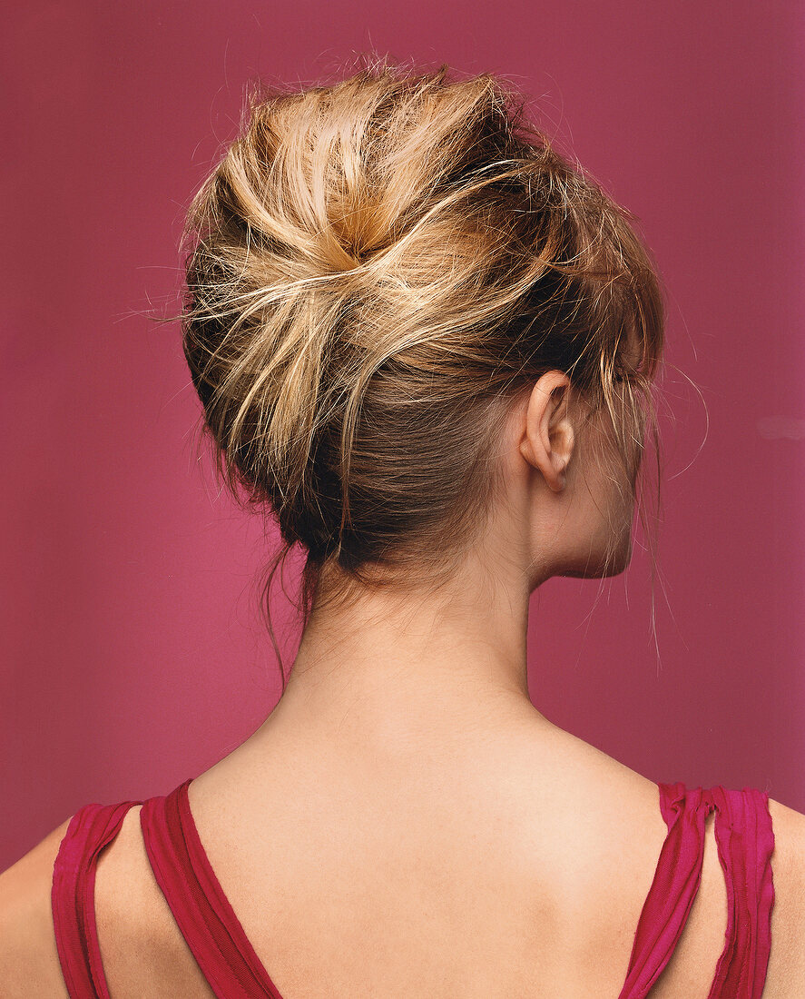 Rear view of blonde woman with updo hair against pink background