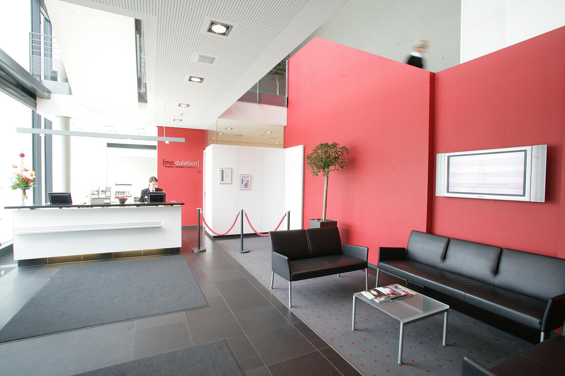 Receptionist standing at reception counter with sitting area in hotel, Germany