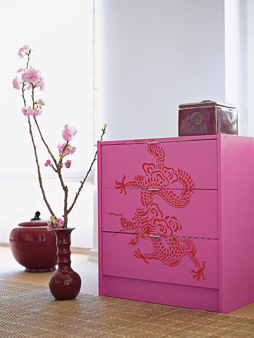 Pink drawer chest with Asian luck symbol next to flower pot on carpet