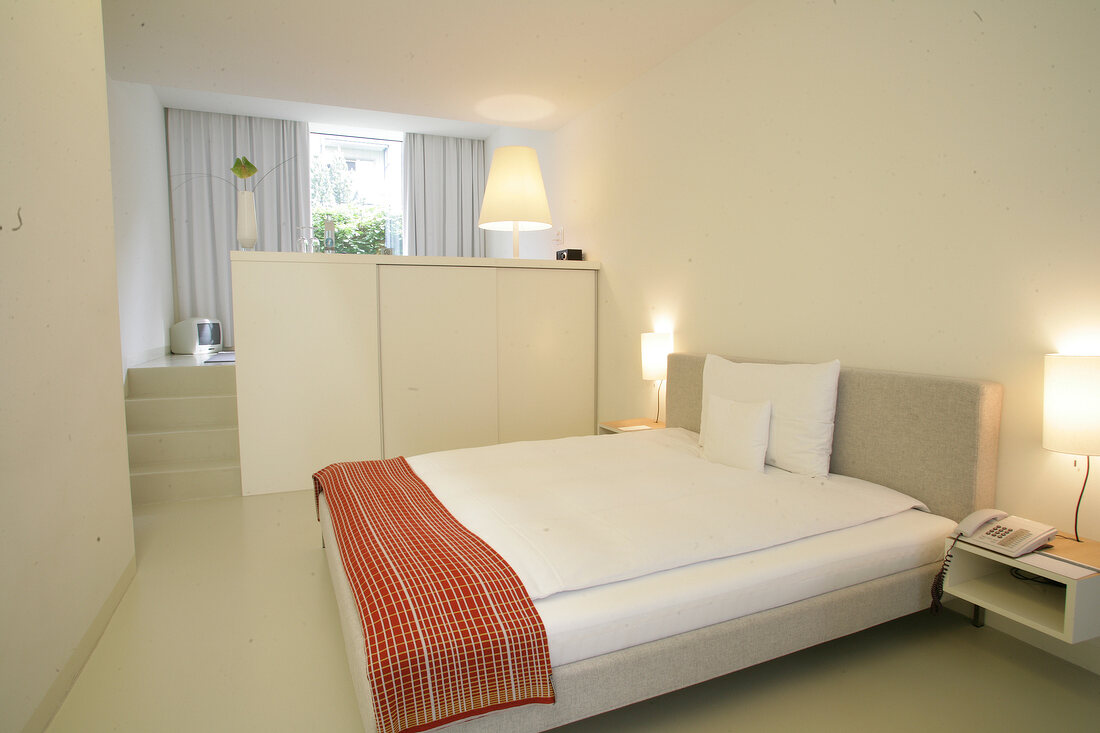 Bedroom with bed, cushion, side lamp and staircase in hotel, Switzerland