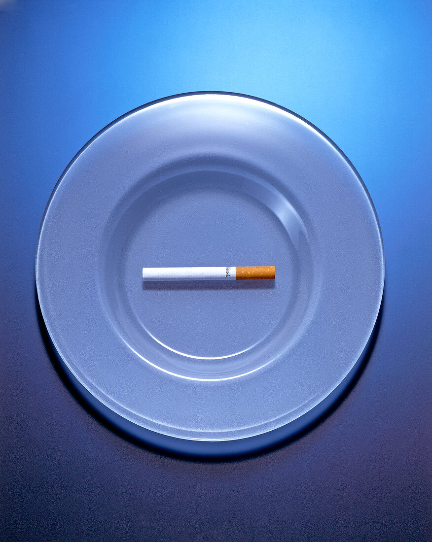 Overhead view of cigarette on a plate against blue background