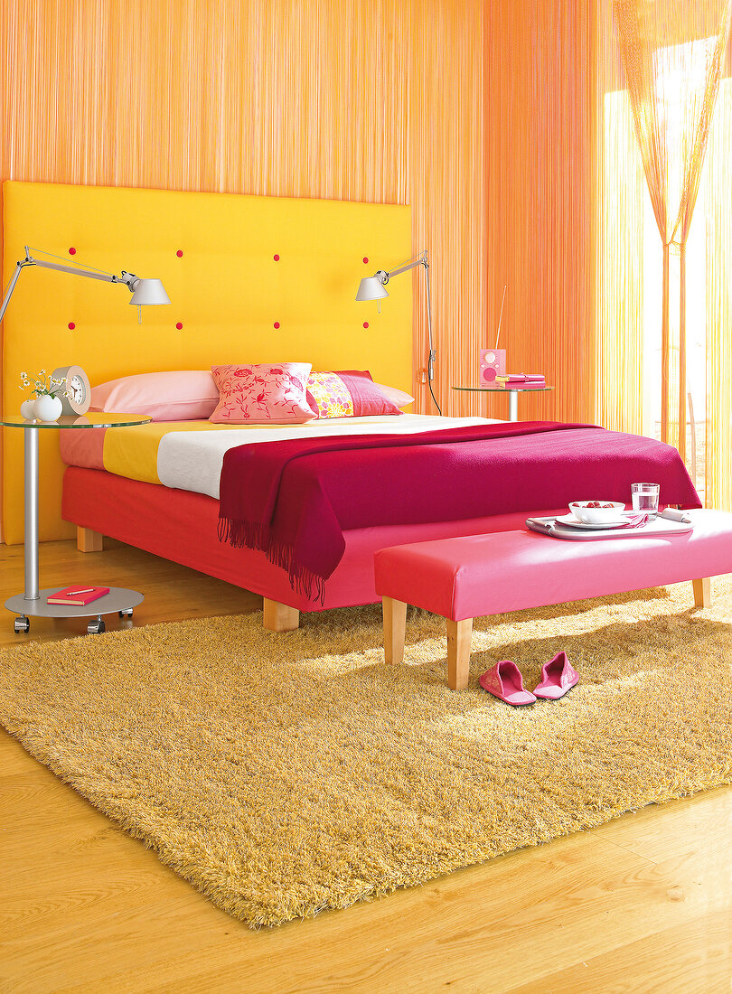 Bedroom with yellow, orange and red bed, stool, rug and curtain