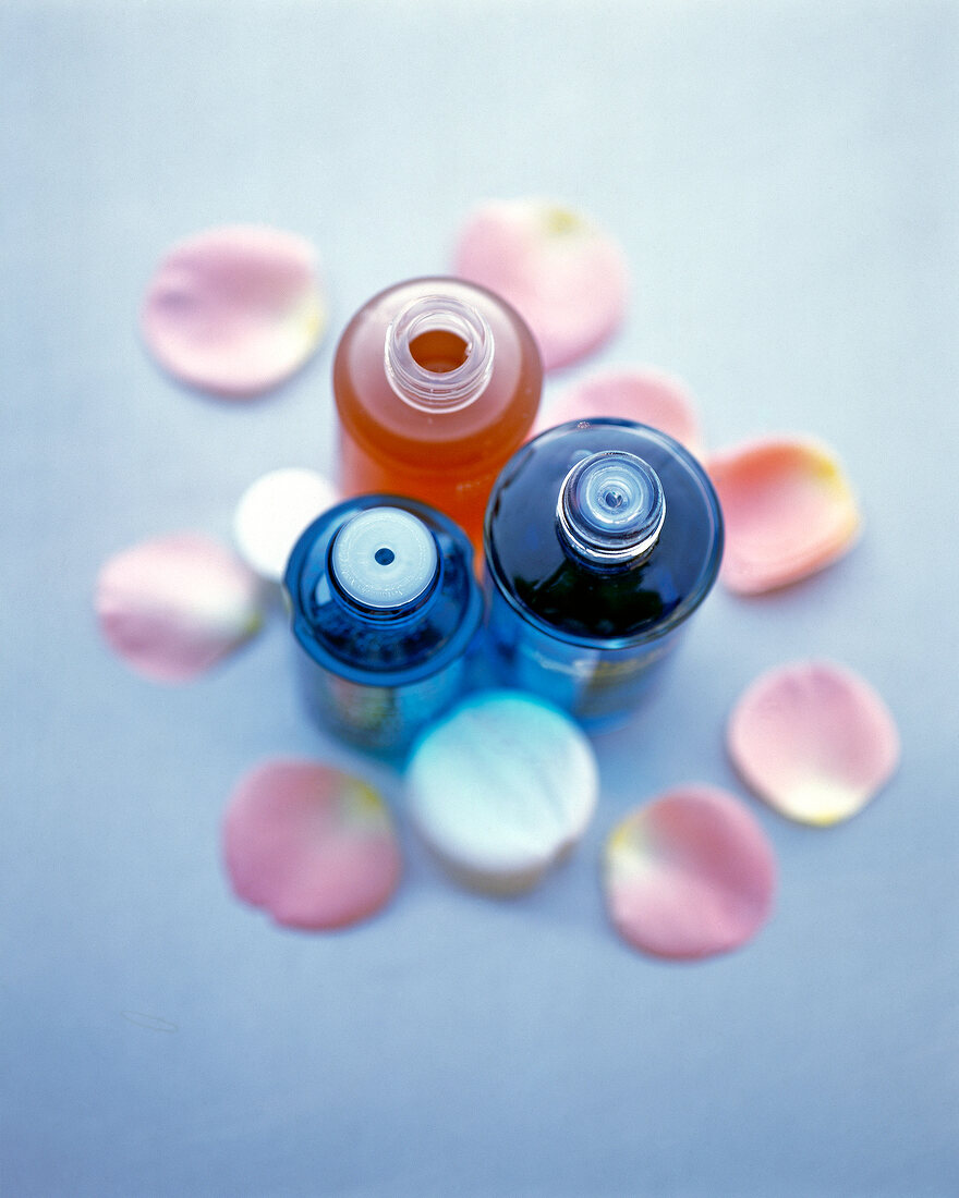 Three bottles of rose water surrounded with rose petals, elevated view