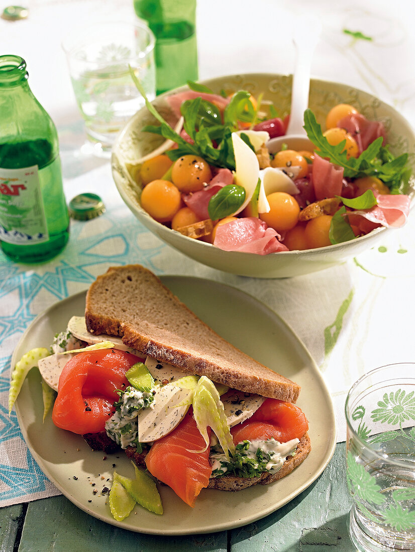 Salmon bread with cream cheese on plate and ham salad with melon in bowl