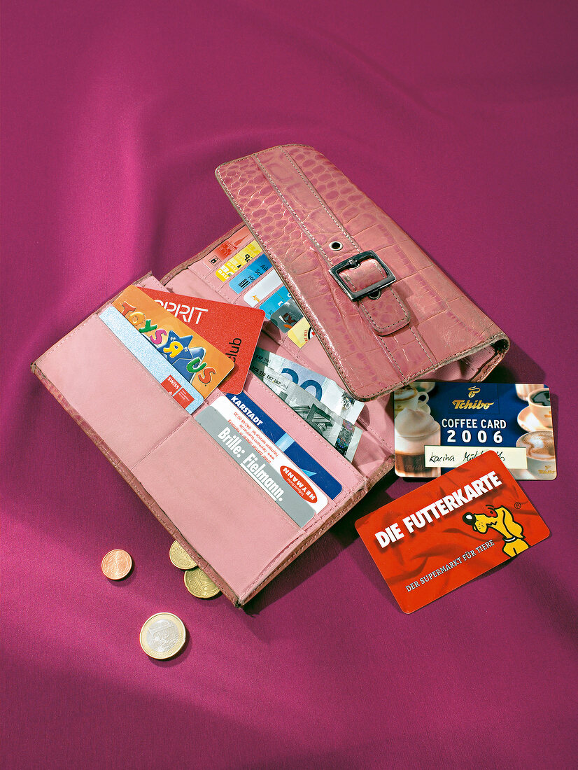 Various cards in pink purse and coins scattered on red background