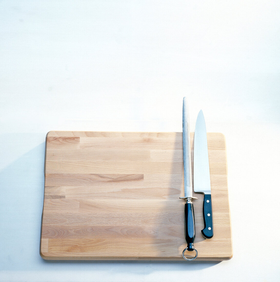 Wooden board with knife and knife sharpener on white background