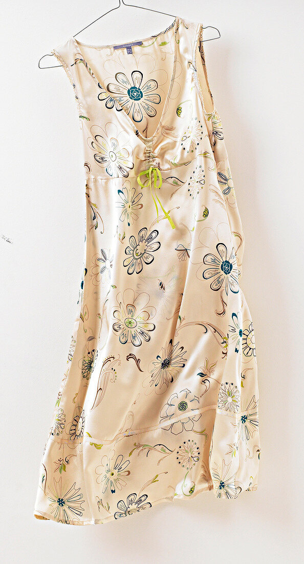 Floral pattern beige silk summer dress hanging on coat hanger