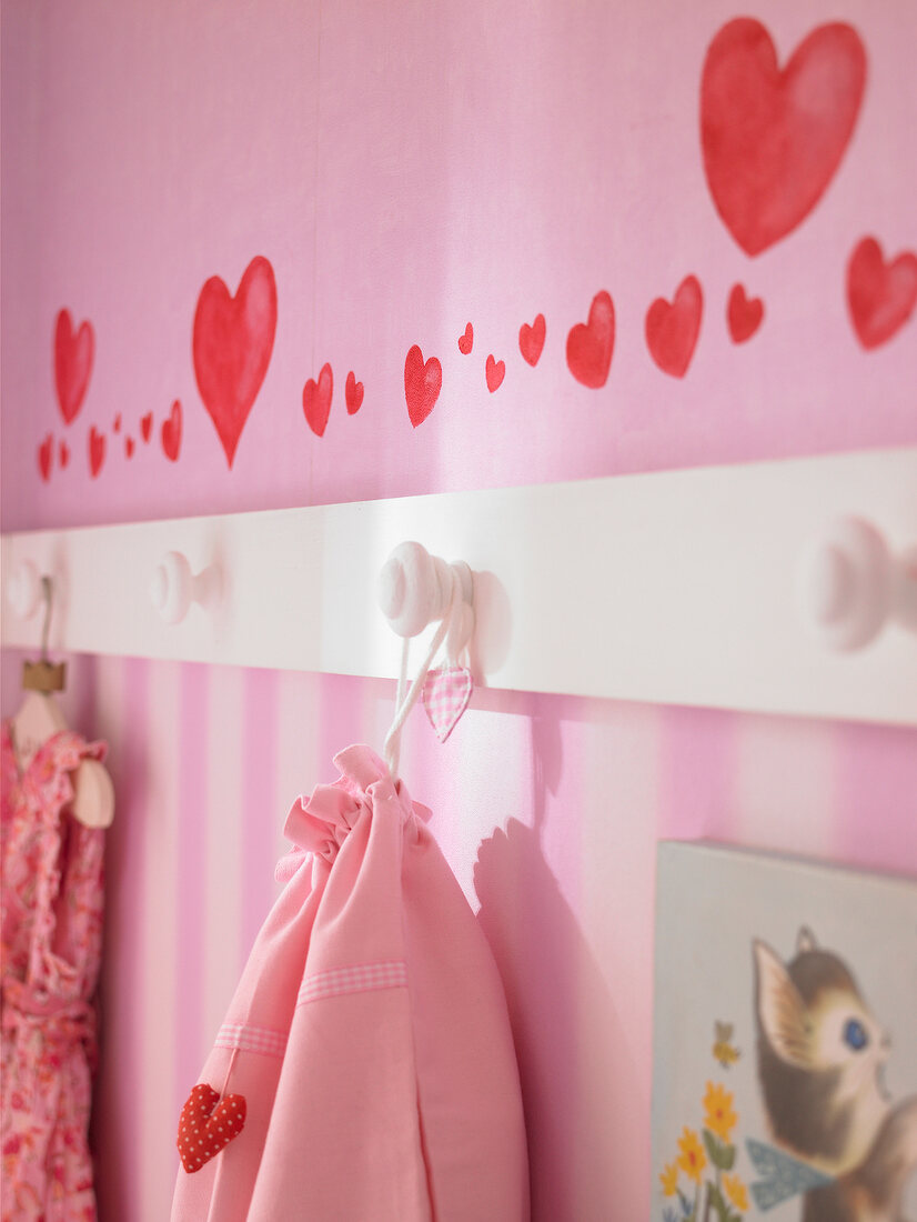 Close-up of white hooks on pink painted wall with hearts drawn