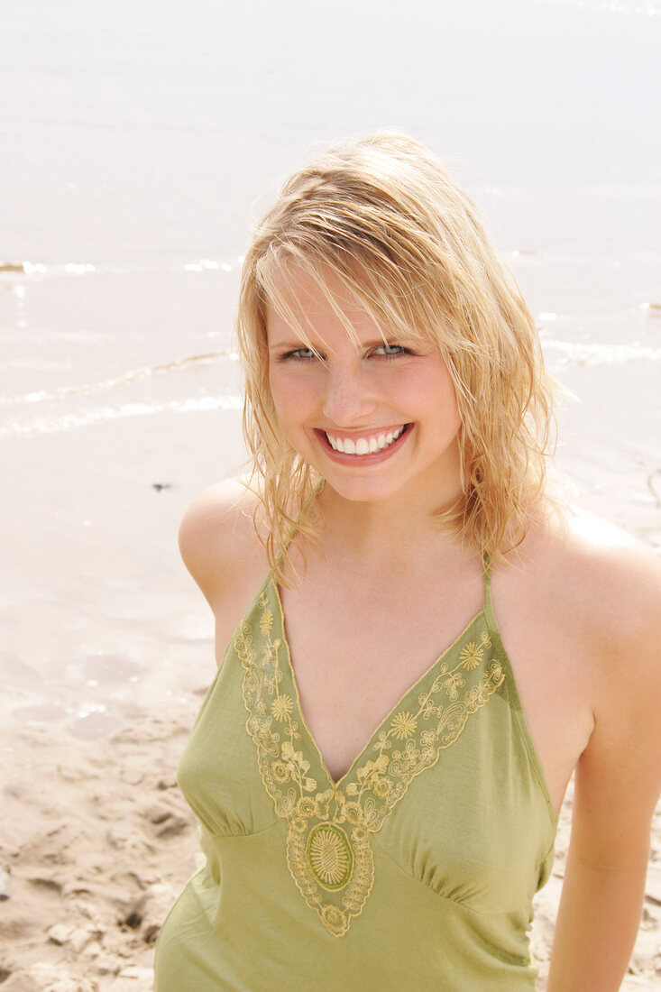 Portrait of beautiful blonde woman wearing green halter top standing on beach, smiling