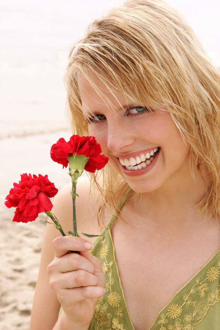 Woman wearing green halterneck dress holding red flower on beach, laughing