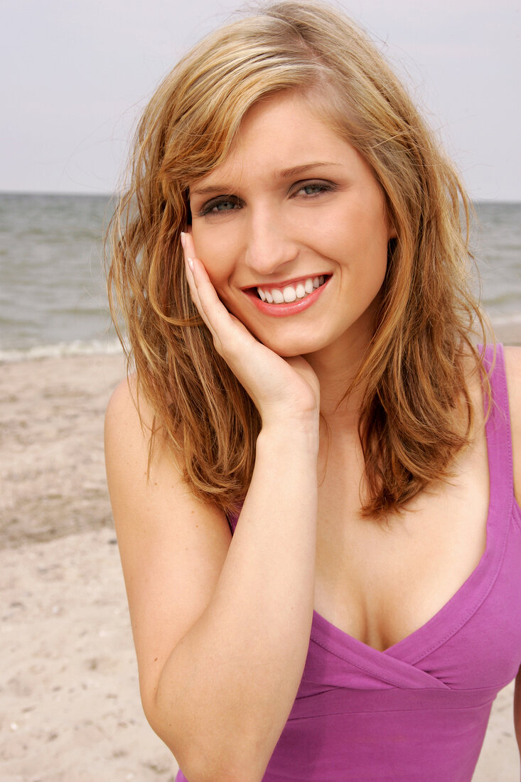 Portrait of beautiful blonde woman wearing pink top standing on beach, smiling